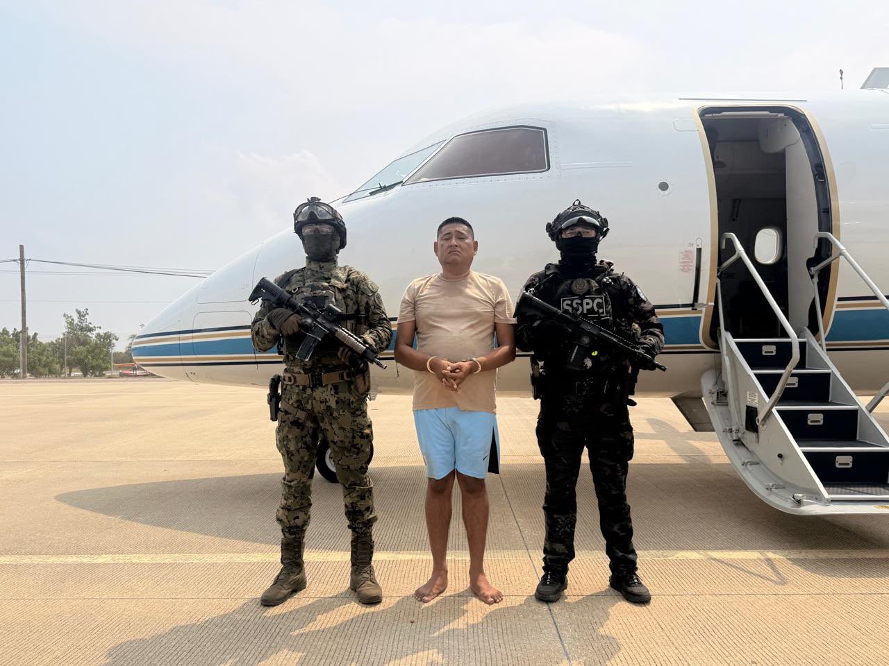 Carlos Alberto "N", alias "La Parca", esposado, custodiado por elementos de la Marina y la SSPC frente a una aeronave