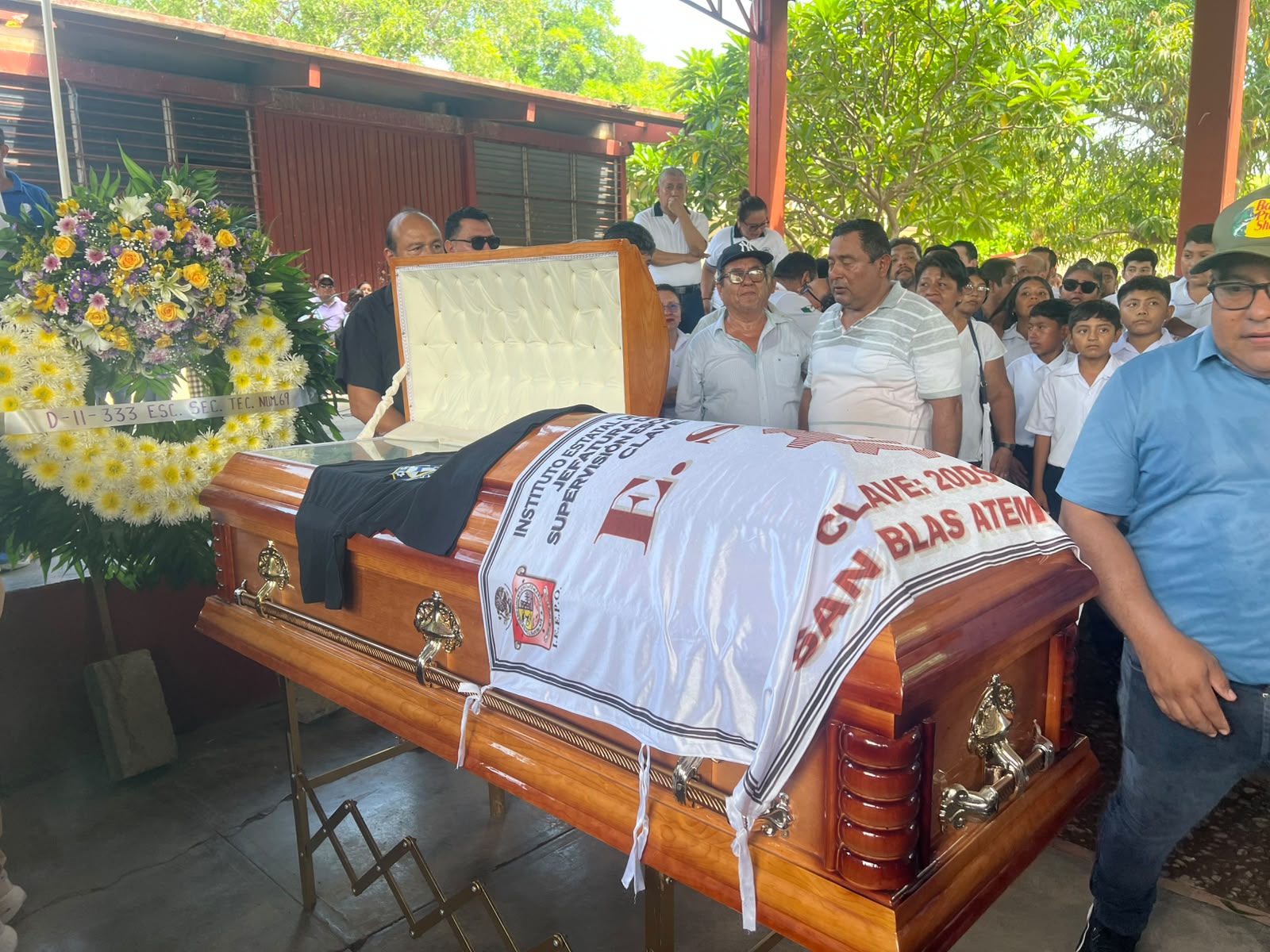 Ataúd del profesor Leví Peralta con ofrendas florales, rodeado de docentes y estudiantes