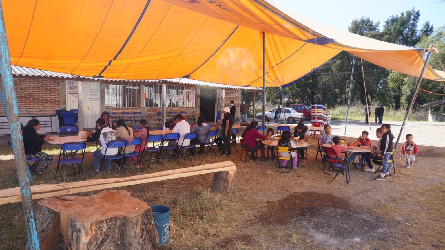 Personas reunidas bajo una carpa naranja, entre ellas niñas y niños