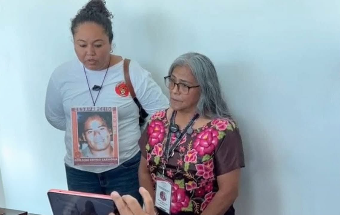 Dos mujeres hablan frente a un celular que graba; una lleva en la blusa la ficha de una persona desaparecida